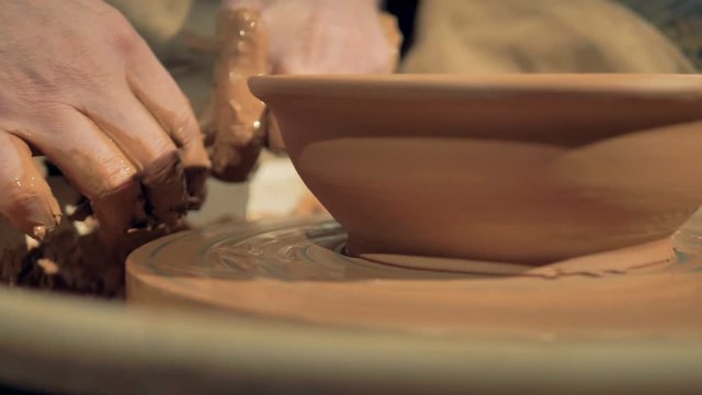 A detailed view on potters hands cutting away excess clay from a bowl. 