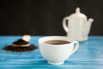 Hot tea next to a spoon with tea leaves on vintage blue board over black background
