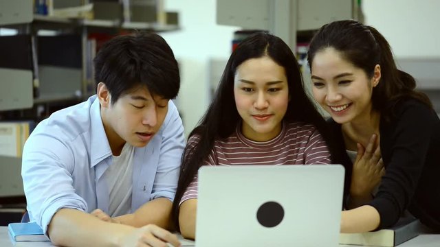 Young students study hard in library. Happy Asian female and male university students doing study research in library with books on desk, notebook. For back to school education diversity concept.