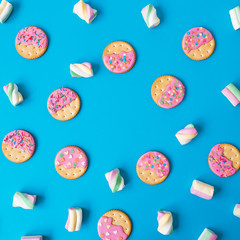 Food frame of cookies with pink glaze and marshmallow on blue background. Flat lay. top view.