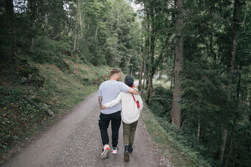 back view of young couple embracing and walking on pathway in green forest