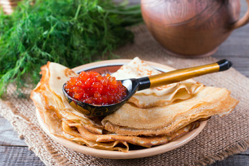 Traditional Russian pancakes with red caviar on wooden rustic background.