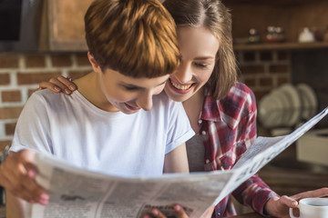 close-up portrait of young lesbian couple reading newspaper together on kitchen