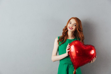 Smiling redhead young holding heart balloon.