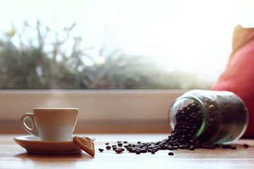 favorite warming drink/ white mug on the background of coffee beans scattered from can on the table by the window