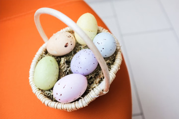 Close-up of Easter basket with pastel painted eggs on bright orange background. 