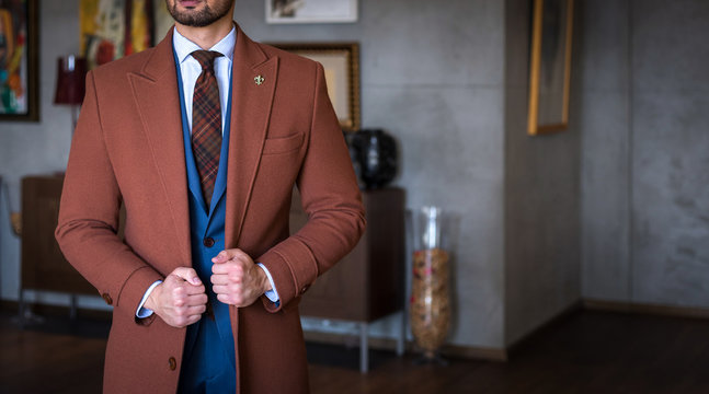 Suited man with tailored trench coat holding his coat and posing indoors