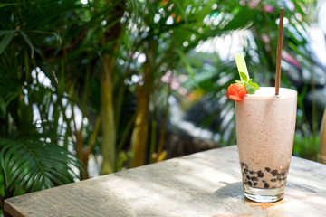 A milkshake with strawberries and jelly, stands on a wooden table on a summer terrace in a cafe. Top view with copy space