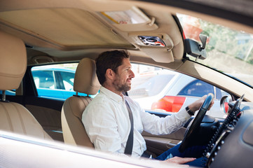 Smiling young man driving his car through city traffic