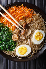 Soba noodles soup with vegetables, shiitake mushrooms, egg and sesame close-up. Vertical top view