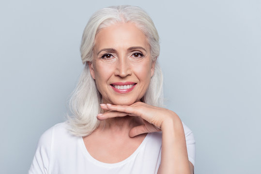 Charming Old Woman Holding Hand Under Chin With Beaming Smile Looking At Camera Over Gray Background