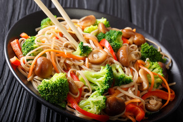 Japanese soba noodles with shiitake mushrooms, broccoli, carrots, peppers close-up on a plate on the table. horizontal