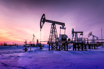 Pump jack, wellhead and pipeline during sunset in the oilfield. Winter period. Oil and gas concept....