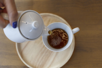 Puring teapot and cup. A hand of woman pouring hot tea into a cup on grey background.