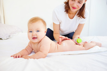 Woman spreading her baby with cream while lying on bed. 
