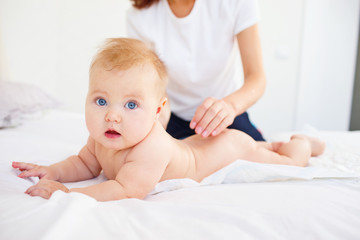 Woman spreading her baby with cream while lying on bed. 