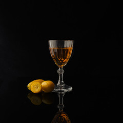 Close-up of a liqueur in a vintage glass with kumquat on a black background