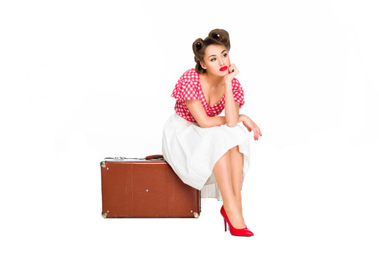 bored beautiful woman in retro clothing sitting on suitcase isolated on white