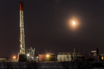 Oil rig during moon eclipse in the oilfield. Winter period. Oil and gas concept. Toned.