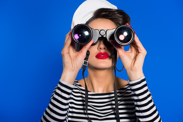 obscured view of attractive young woman in retro clothing with binoculars isolated on blue