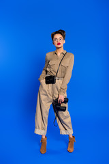 stylish young woman with binoculars and photo camera isolated on blue