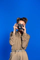 obscured view of fashionable young woman in retro clothing with photo camera isolated on blue