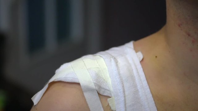 The man shows a gauze bandage superimposed on his right shoulder. The dressing is fixed with adhesive plaster.