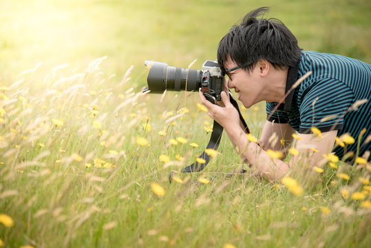 Young Asian male photographer taking photo by DSLR camera on green field. Nature and landscape photography