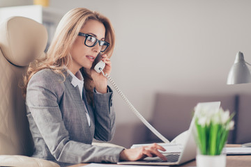 Portrait of successful, stylish, attractive, pretty, thoughtful businesswoman in glasses talking on phone with colleague, using laptop for work, having business phone conversation