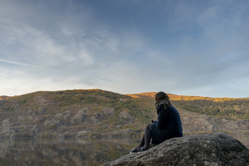 Woman sitting on a big rock on the edge of a glacier lake. Sanabria Lake.
