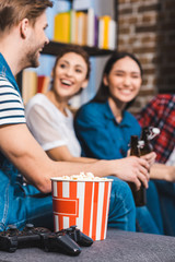 close-up view of joysticks and popcorn in box and young friends sitting behind