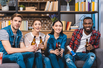 happy young multiethnic friends drinking beer while sitting together on sofa