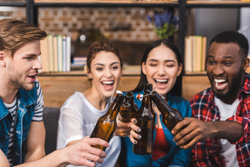 happy young multiethnic friends clinking beer bottles