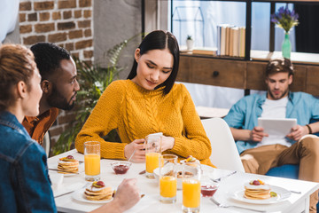 cropped shot of multiethnic friends looking at asian girl using smartphone at table and young man using digital tablet behind