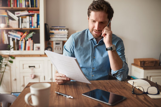 Man Talking On A Cellphone While Reading Paperwork At Home