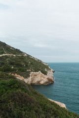 Fototapeta na wymiar Colina de montaña con camino con vistas al mar nublado