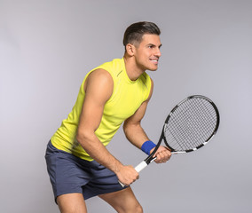 Portrait of handsome man playing tennis against grey background