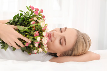 Beautiful young woman with bouquet of roses on bed at home