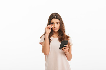 Upset brunette woman in t-shirt holding smartphone