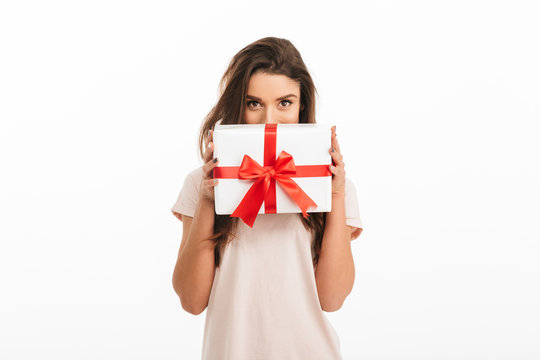 Playful brunette woman in t-shirt hiding behind gift box