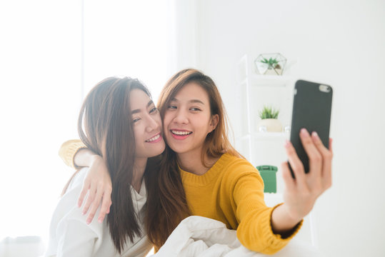 Beautiful young asian women LGBT lesbian happy couple sitting on bed hug and using phone taking selfie together bedroom at home. LGBT lesbian couple together indoors concept. Spending nice time home.