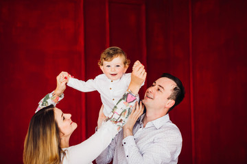 Mom, dad and their little son dressed in casual style pose in a red room