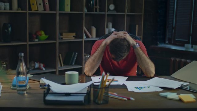 Upset business man putting hands on head. Depressed man thinking about business in office at night. Thinking businessman at desk in cozy office. Tired man put hands on head at desk in home workplace