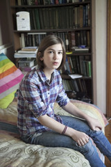 the A thoughtful girl in a plaid shirt is sitting on the bed in front of a bookcase