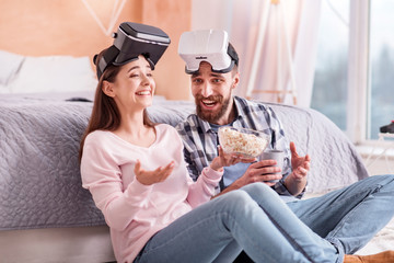 Funny story. Jolly cute merry couple in VR glasses nickering while sitting and woman holding popcorn