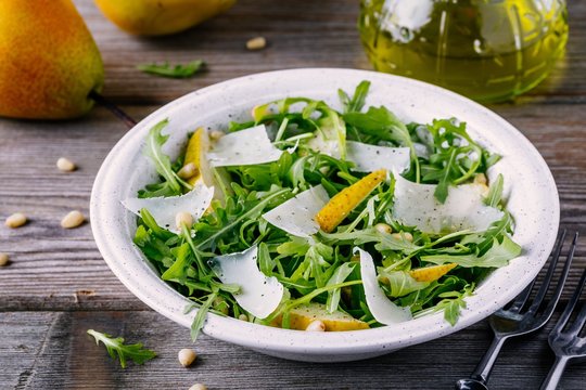 green salad bowl of arugula with pear, parmesan cheese and pine nuts