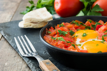 Shakshuka in iron frying pan on wooden table. Typical food in Israel.