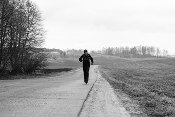 A sportsman is running on a higway in countryside landscape.