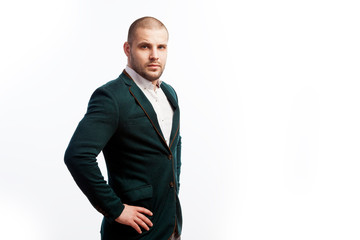 A young bald man in a white shirt, green suit confidently looks at the camera and holds his hands on his jacket on a white isolated background, side view