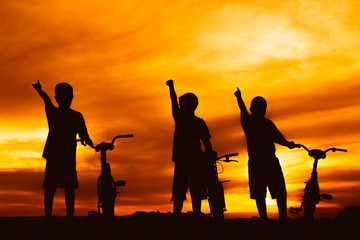 Fototapeta premium silhouette boys riding bicycle at sunset or sunrise background